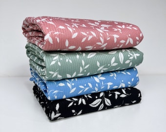 May include: Four different fabric swatches with a white leaf pattern on a pink, green, blue, and black background. The fabric is ribbed and has a soft texture.