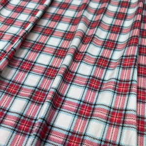 Puede incluir: Tela blanca con un patrón de cuadros rojos, rosados y azules. La tela está doblada y tiene una textura suave.