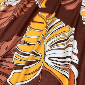 May include: Close-up of brown fabric with a yellow, white, and brown leaf pattern.