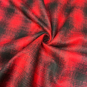 K&ouml;nnte beinhalten: Roter und schwarzer karierter Flanellstoff mit weicher, flauschiger Textur. Der Stoff ist gefaltet und drapiert, wodurch Muster und Textur sichtbar werden.