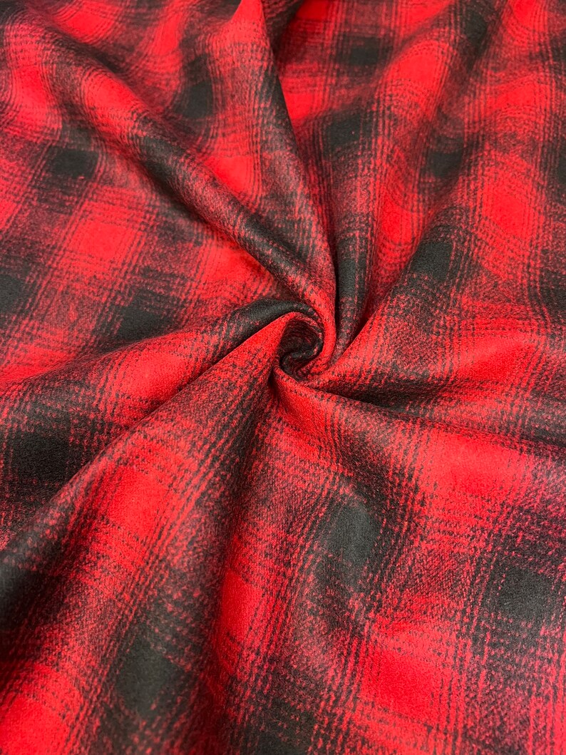 K&ouml;nnte beinhalten: Roter und schwarzer karierter Flanellstoff mit weicher, flauschiger Textur. Der Stoff ist gefaltet und drapiert, wodurch Muster und Textur sichtbar werden.