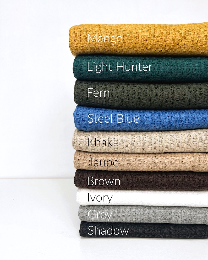 Puede incluir: Una pila de 10 muestras de tejido de punto de gofre en varios colores, incluyendo mango, cazador claro, helecho, azul acero, caqui, topo, marr&oacute;n, marfil, gris y sombra.