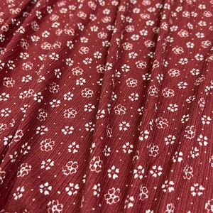 May include: Close-up of a burgundy fabric with a white floral pattern. The fabric has a ribbed texture.