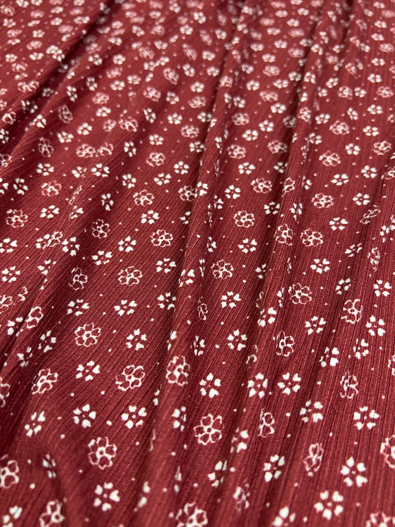 May include: Close-up of a burgundy fabric with a white floral pattern. The fabric has a ribbed texture.