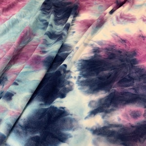 May include: A close-up of a tie-dye fabric with shades of blue, purple, and white. The fabric has a soft, flowing texture and a unique, abstract pattern.