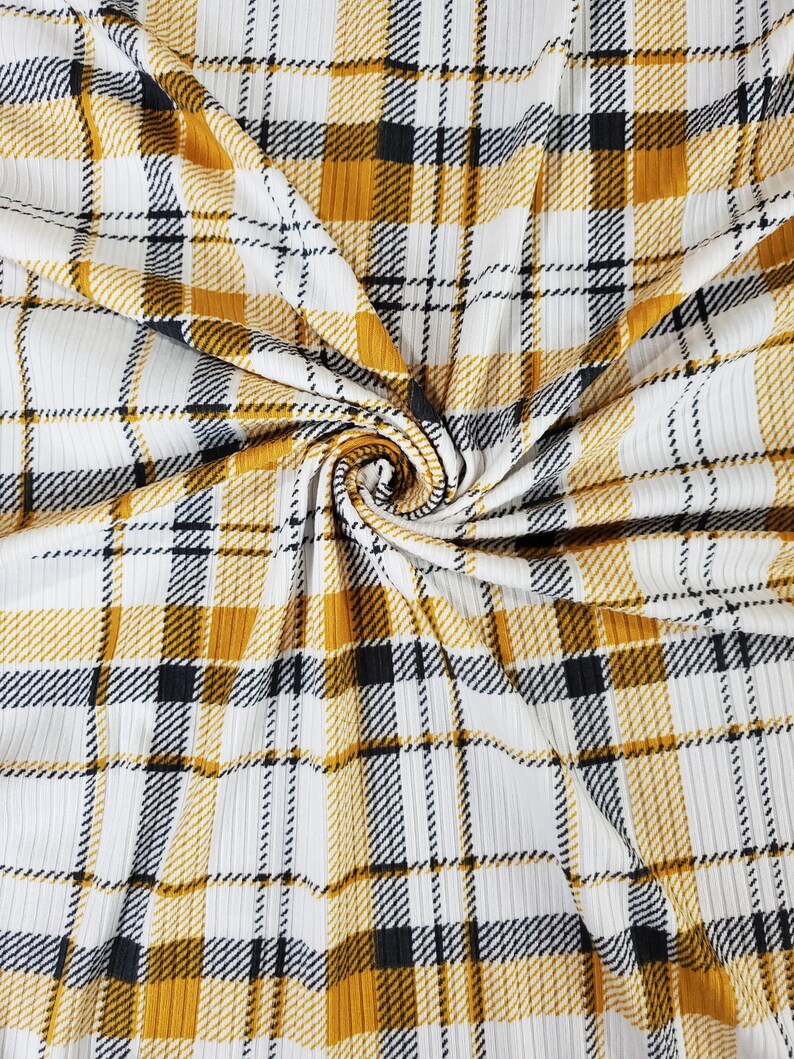 May include: White fabric with a yellow and black plaid pattern. The fabric has a ribbed texture.