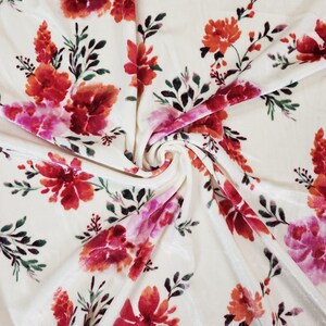 May include: White velvet fabric with a pink, red, and orange floral print. The fabric is soft and luxurious, ideal for upholstery or clothing.