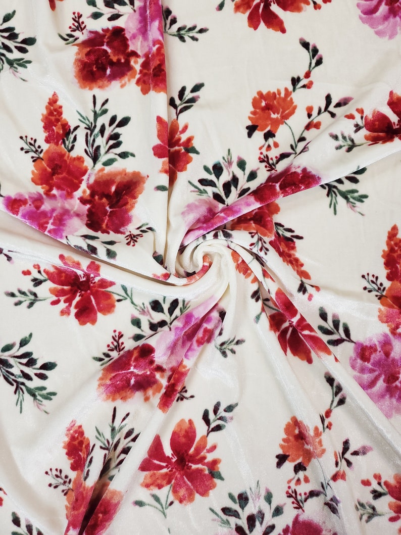 May include: White velvet fabric with a pink, red, and orange floral print. The fabric is soft and luxurious, ideal for upholstery or clothing.