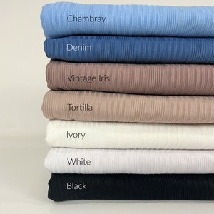 May include: A stack of seven fabric swatches in various colours, including black, white, ivory, tortilla, vintage iris, denim, and Chambray.