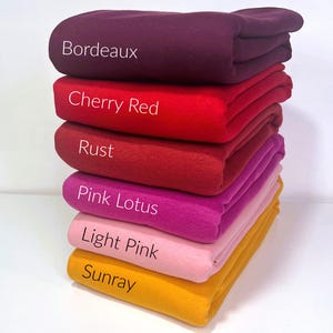 May include: A stack of six fabric swatches in different shades of red, pink, and yellow. The swatches are labeled "Bordeaux", "Cherry Red", "Rust", "Pink Lotus", "Light Pink", and "Sunray".