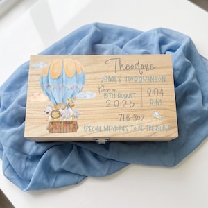 May include: A rectangular wooden keepsake box featuring a printed illustration of a light blue hot air balloon carrying cartoon animals. The text reads Theodore James Hodgkinson, Born on 15th August 2025, 9:04 A.M., 7lb 3oz, and Special Memories to be Treasured.