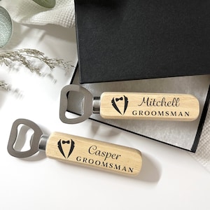May include: Two wooden bottle openers with a tuxedo design and the words "Groomsman" and the names "Mitchell" and "Casper" engraved on them.