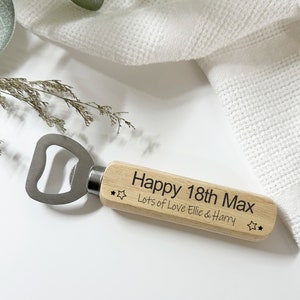 May include: Wooden bottle opener with a metal opener and a personalised message that reads "Happy 18th Max Lots of Love Ellie & Harry" with two stars on either side of the message.