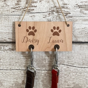 May include: Wooden dog lead holder with two hooks and paw prints. The holder has the names "Daisy" and "Luna" engraved on it.