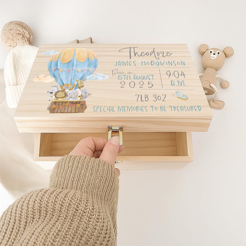 May include: A rectangular wooden keepsake box with a metal latch, featuring a watercolor illustration of a blue hot air balloon with animals, and printed text: Theodore, James Hodgkinson, Born on 15th August 2025, 9:04 A.M., 7LB 3OZ, SPECIAL MEMORIES TO BE TREASURED.