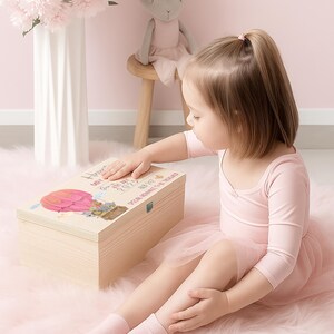 May include: A rectangular light-colored wooden keepsake box featuring a printed illustration of a pink hot air balloon and text that reads "Born on 6th May 2025" and "Special Memories To Be Treasured" with a silver metal latch on the front.