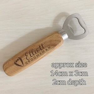 May include: Wooden bottle opener with a metal cap opener. The handle is engraved with the name "Elliott" and the words "Groomsman". The bottle opener measures approximately 14 inches by 3 inches and is 2 inches deep.
