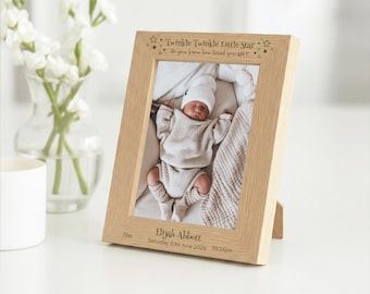 May include: A light-colored wooden picture frame with the text "Twinkle Twinkle Little Star" and a photo of a newborn baby. The baby is wearing a white hat and a light-colored sweater. The frame also includes the baby's name, birth date, and weight.
