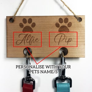 Pu&ograve; includere: Porta-guinzagli per cani in legno con due ganci e impronte di zampe. Il porta-guinzagli &egrave; personalizzato con i nomi "Alfie" e "Pip".