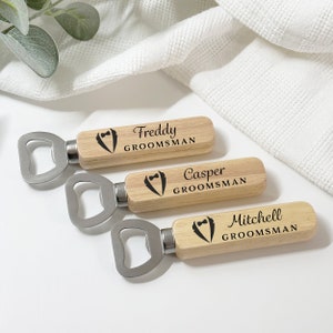 May include: Three wooden bottle openers with metal bottle opener heads. Each opener has a tuxedo graphic and the text "GROOMSMAN" with a name above it. The names are Freddy, Casper, and Mitchell.