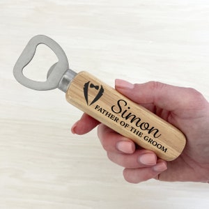 May include: Wooden bottle opener with a silver bottle opener head. The handle is engraved with the text "Simon Father of the Groom" and a tuxedo icon.