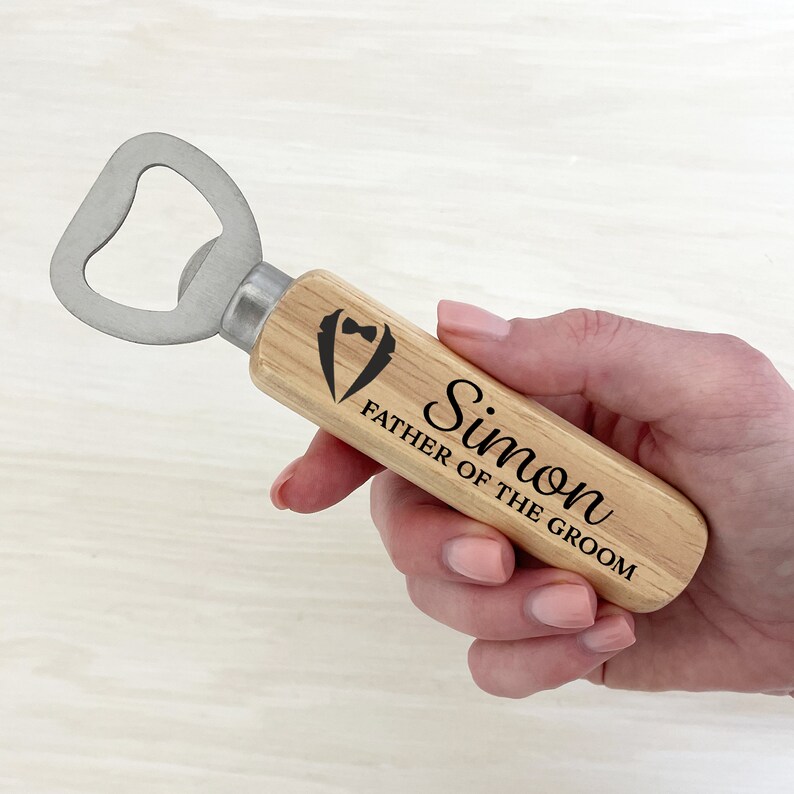 May include: Wooden bottle opener with a silver bottle opener head. The handle is engraved with the text "Simon Father of the Groom" and a tuxedo icon.