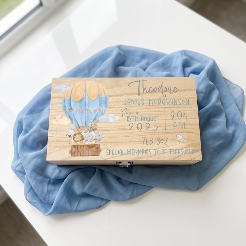 May include: A rectangular wooden keepsake box featuring a printed illustration of a light blue hot air balloon carrying cartoon animals. The text reads Theodore James Hodgkinson, Born on 15th August 2025, 9:04 A.M., 7LB 3OZ, and Special Memories to be Treasured.
