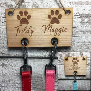 Pu&ograve; includere: Porta-guinzagli per cani in legno con due ganci e disegni di impronte di zampe. Il porta-guinzagli &egrave; inciso con i nomi "Teddy" e "Maggie".