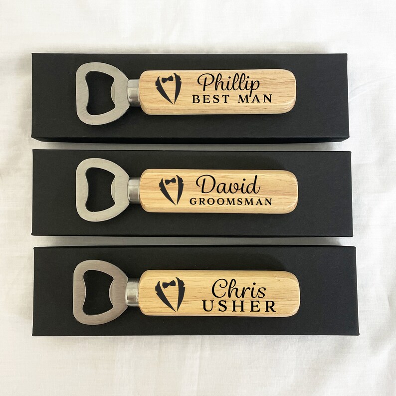 May include: Three wooden bottle openers with a silver bottle opener head. Each opener has a tuxedo graphic and personalized text. The top opener says "Phillip Best Man", the middle opener says "David Groomsman", and the bottom opener says "Chris Usher".