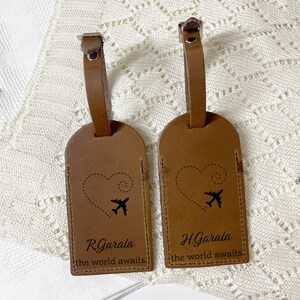 May include: Two brown leather luggage tags with silver buckles. Each tag has a black airplane and heart design, with the text "R. Garala the world awaits" and "H. Garala the world awaits."