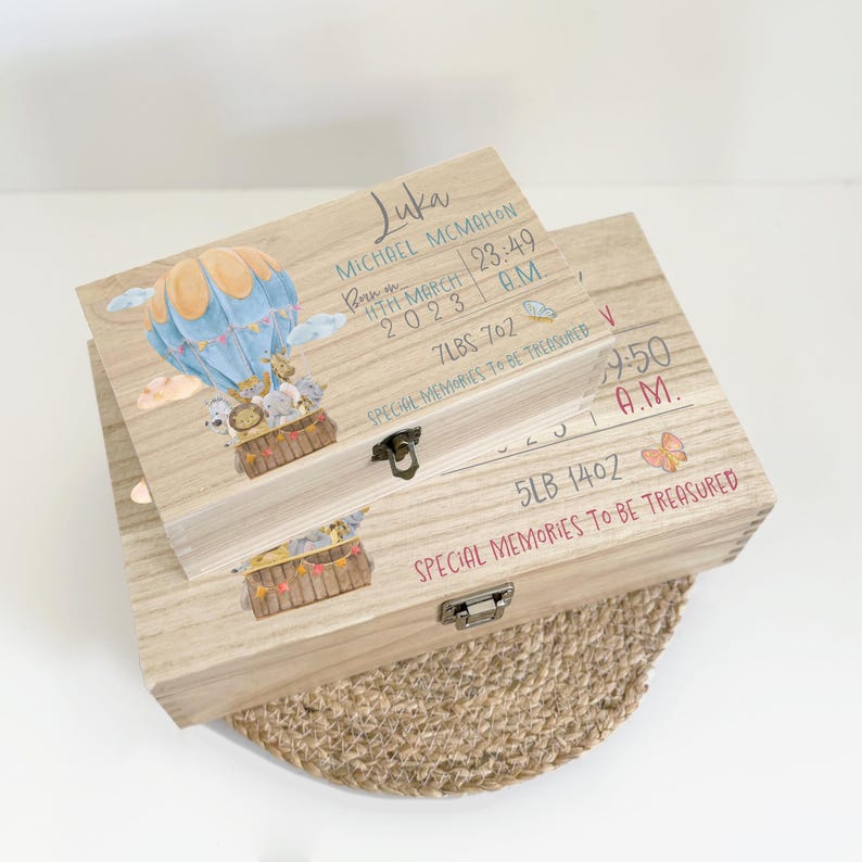 May include: Two rectangular wooden keepsake boxes with metal latches. The top box features a watercolor hot air balloon with animals, the name Luka, birth date 11th March 2023, time 23:49, and weight 7lbs 7oz. Both boxes have the text Special Memories To Be Treasured.