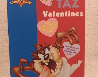 May include: A box of 32 Taz Valentines featuring a cartoon image of Taz the Tasmanian Devil. The box is red and pink with the text "32 Taz Valentines" and "Fun Activities on every card!" The back of the box has card designs printed on it.