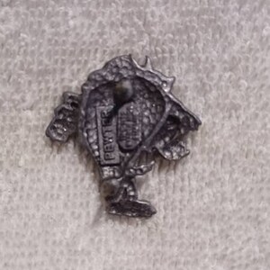 May include: A small, detailed pewter figurine of a creature with a textured surface. The figurine is on a white, textured surface. The word "PEWTER" is visible on the figurine.