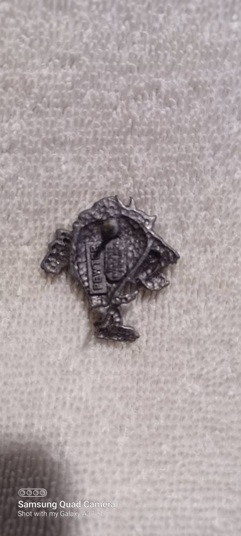 May include: A small, detailed pewter figurine of a creature with a textured surface. The figurine is on a white, textured surface. The word "PEWTER" is visible on the figurine.
