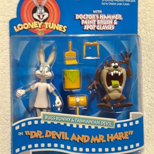 May include: A Looney Tunes action figure set featuring Bugs Bunny and the Tasmanian Devil in "Dr. Devil and Mr. Hare." The set includes figures and accessories like a hammer, paint brush, and spot glasses, all packaged in a blue blister pack.