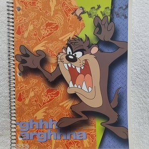 May include: Spiral-bound notebook featuring the Tasmanian Devil cartoon character. The cover has a colorful design with the character's image, the words "ghhh arghhna", and a patterned background in orange and blue.