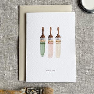 A watercolour new home card with a minimal design featuring three paint brushes.