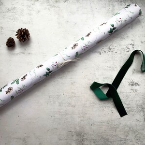 May include: A roll of white wrapping paper with a green and red holly pattern. A green velvet ribbon and two pine cones are also included.
