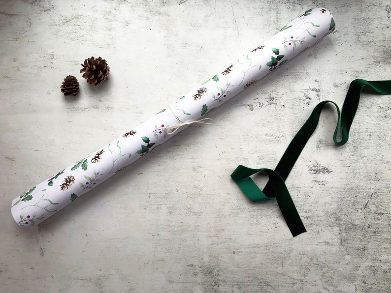 May include: A roll of white wrapping paper with a green and red holly pattern. A green velvet ribbon and two pine cones are also included.