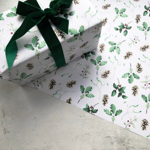 May include: A white gift box wrapped in paper with a green and brown holly and pine cone pattern. A green velvet ribbon is tied around the box with a bow.