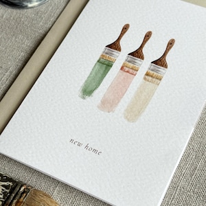 Close up of watercolour new home card featuring three paint brushes dipped into neutral paints.