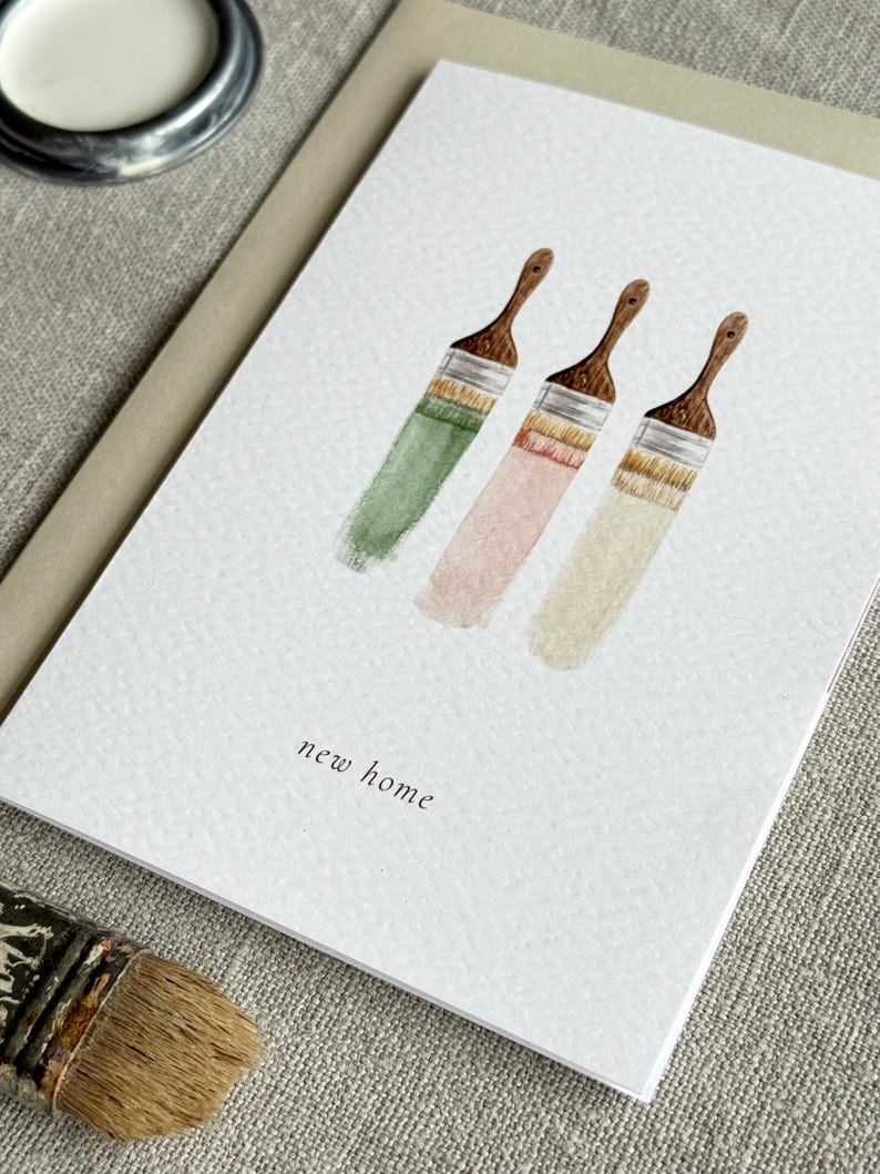 Close up of watercolour new home card featuring three paint brushes dipped into neutral paints.