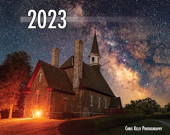 May include: A stone church with a spire under a night sky with the Milky Way galaxy visible. The year 2023 is written in white text across the top of the image. The text "Chris Kelly Photography" is at the bottom of the image.