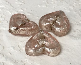 May include: Three pink glass heart-shaped beads with silver flecks. The beads are translucent and have a slightly iridescent sheen.