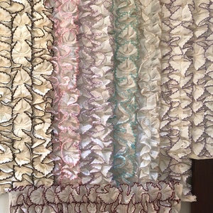 May include: A close-up of six white fabric trims with different colored stitching. The trims have a ruffled design and are arranged in a row.
