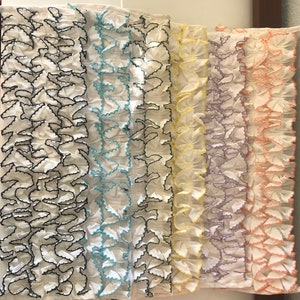 May include: Five white fabric strips with different colored ruffled edges. The edges are black, light blue, yellow, lavender, and peach.