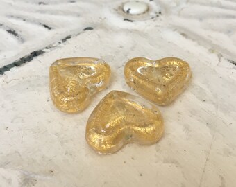 May include: Three gold glass heart-shaped ornaments with a metallic finish.