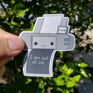 May include: A gray and white cartoon printer sticker with a smiling face and the text "I am out of ink".