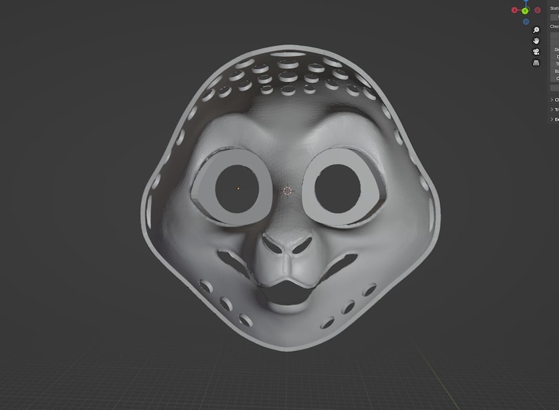 May include: A gray, stylized mask with large eye openings and a small nose and mouth. The mask has a series of small holes around the edges and top. The overall shape is rounded, resembling a cartoon character.