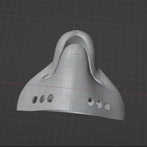 May include: A light gray, 3D-rendered object with a curved, helmet-like shape. It features a series of small, circular holes along the bottom edge and a raised, arched section at the top. The object is set against a dark gray grid background.